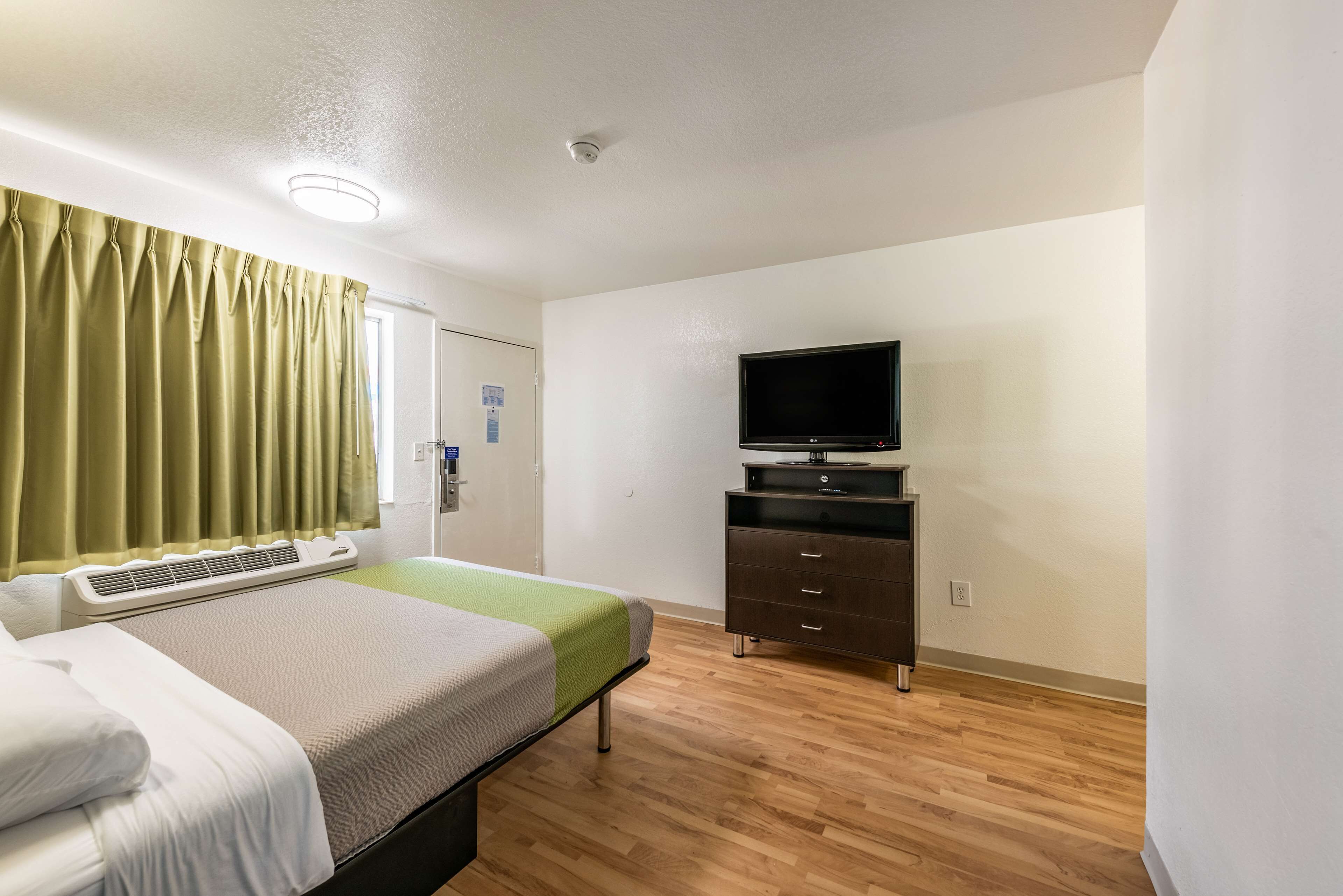 Une chambre d’hôtel avec un lit, une télévision, une commode et une fenêtre avec des rideaux.