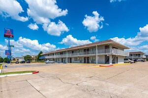 A motel with a two-story building, a balcony on the second floor, and a parking lot with several cars.