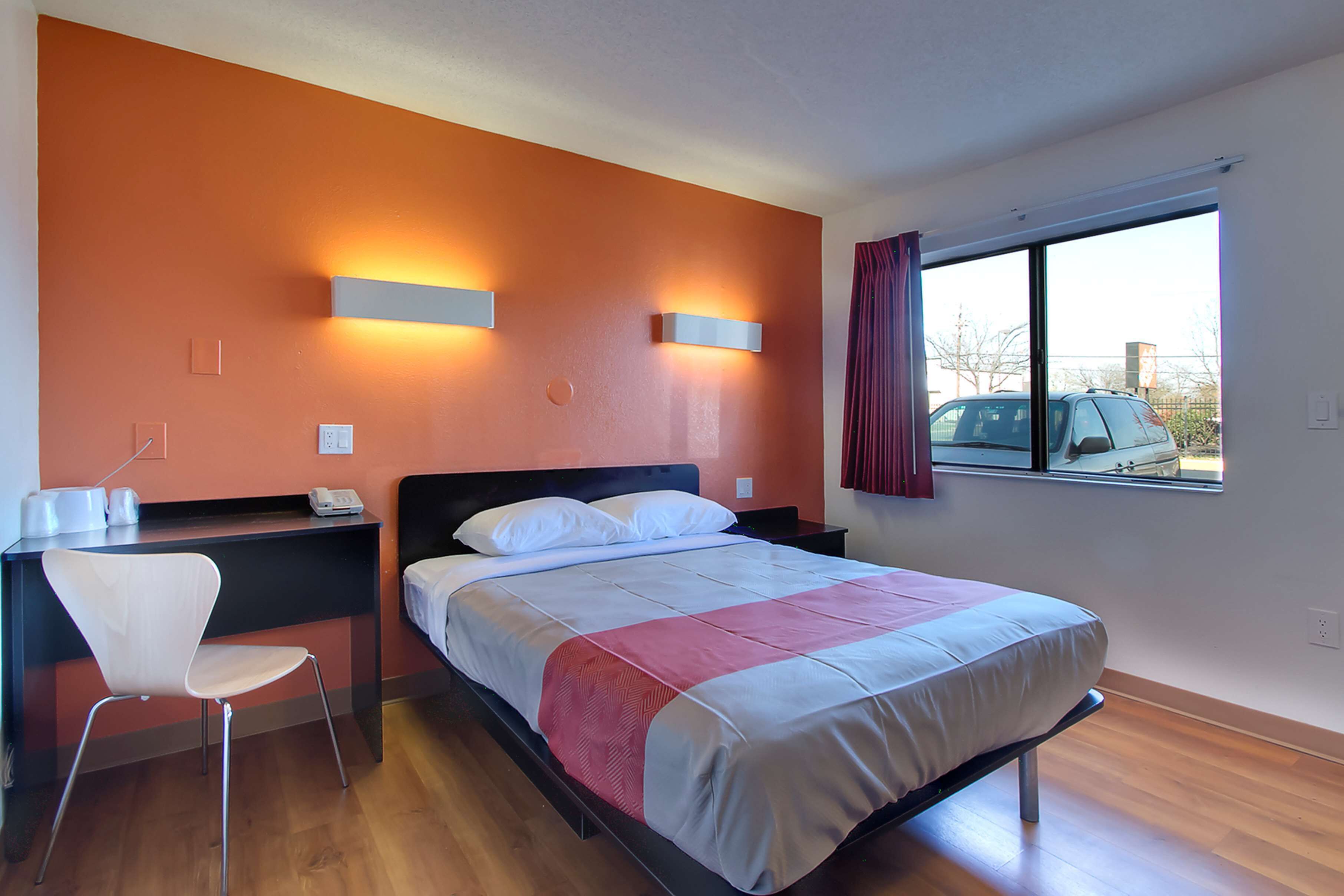 A hotel room with a bed, a desk, a chair, and a window with a view of the outside.