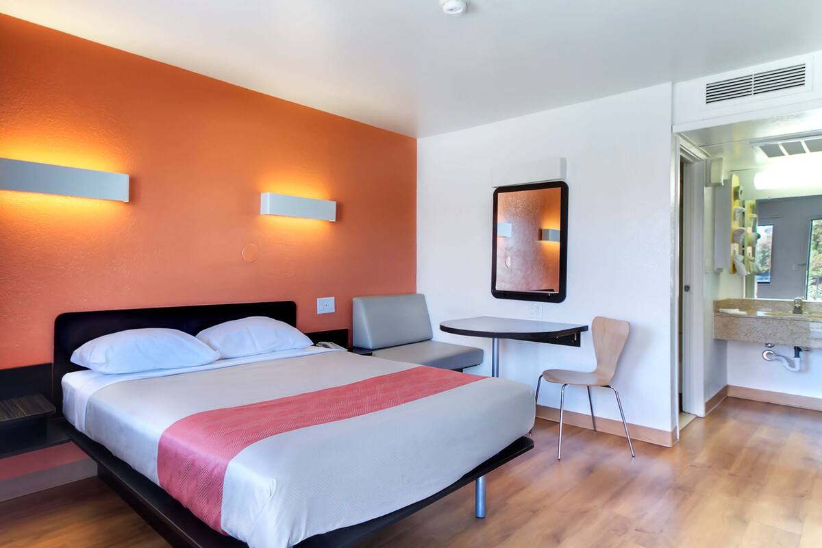 Une chambre d’hôtel comprenant un lit, un bureau, une chaise et une salle de bain avec un lavabo et un miroir.