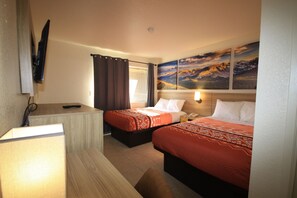 A hotel room with two beds, a desk, a flat-screen TV, and a painting of mountains on the wall.