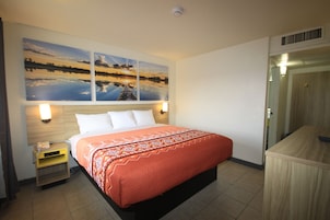 Habitación de hotel con cama, mesita de noche, teléfono en la pared y puerta con espejo.