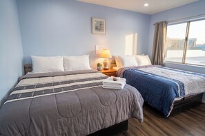 Ein Hotelzimmer mit zwei Betten, einem Nachttisch mit Lampe, einer kleinen Pflanze und einem Fenster mit Vorhängen.