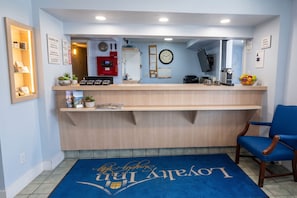 Zona de recepción con alfombra azul, mostrador de recepción, un reloj y una silla.