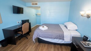 Habitación de hotel con cama, escritorio, silla, televisor y mesita de noche con lámpara.