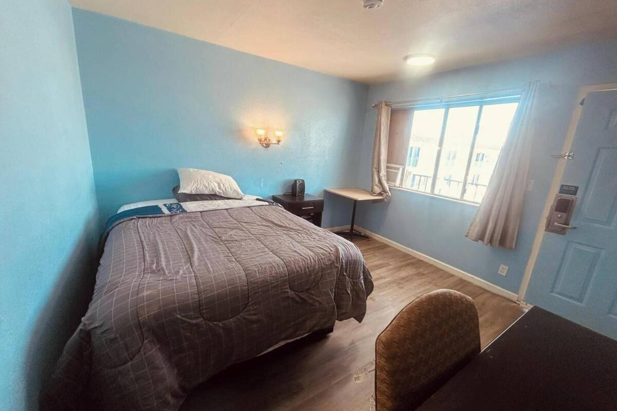 A bedroom with a bed, a desk, a chair, and a window with curtains.