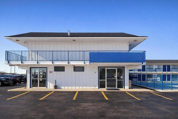 Un motel à deux étages, à l’extérieur blanc et aux accents bleus, doté d’un parking et d’une piscine visible à l’arrière-plan.