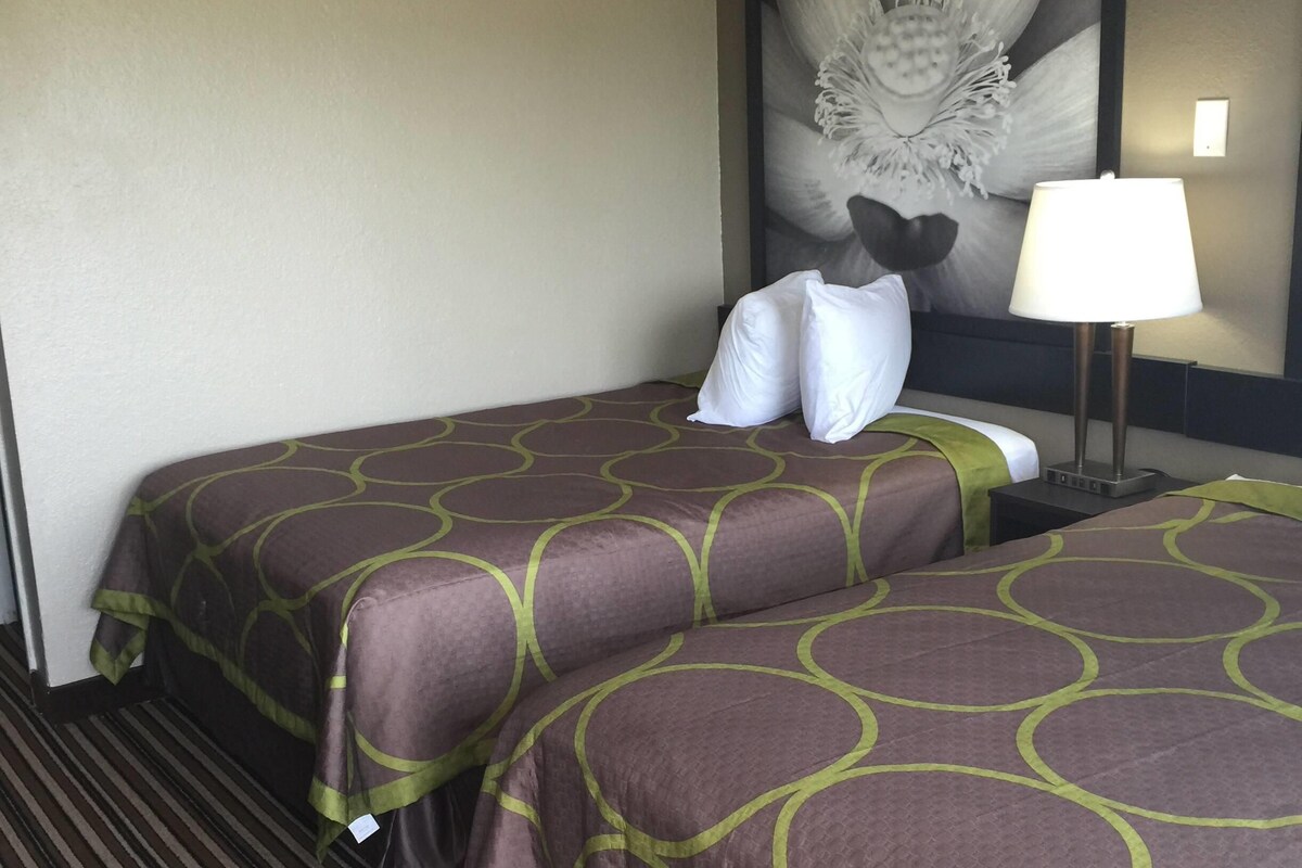 A hotel room with two beds, a nightstand, a lamp, and a large abstract painting on the wall.