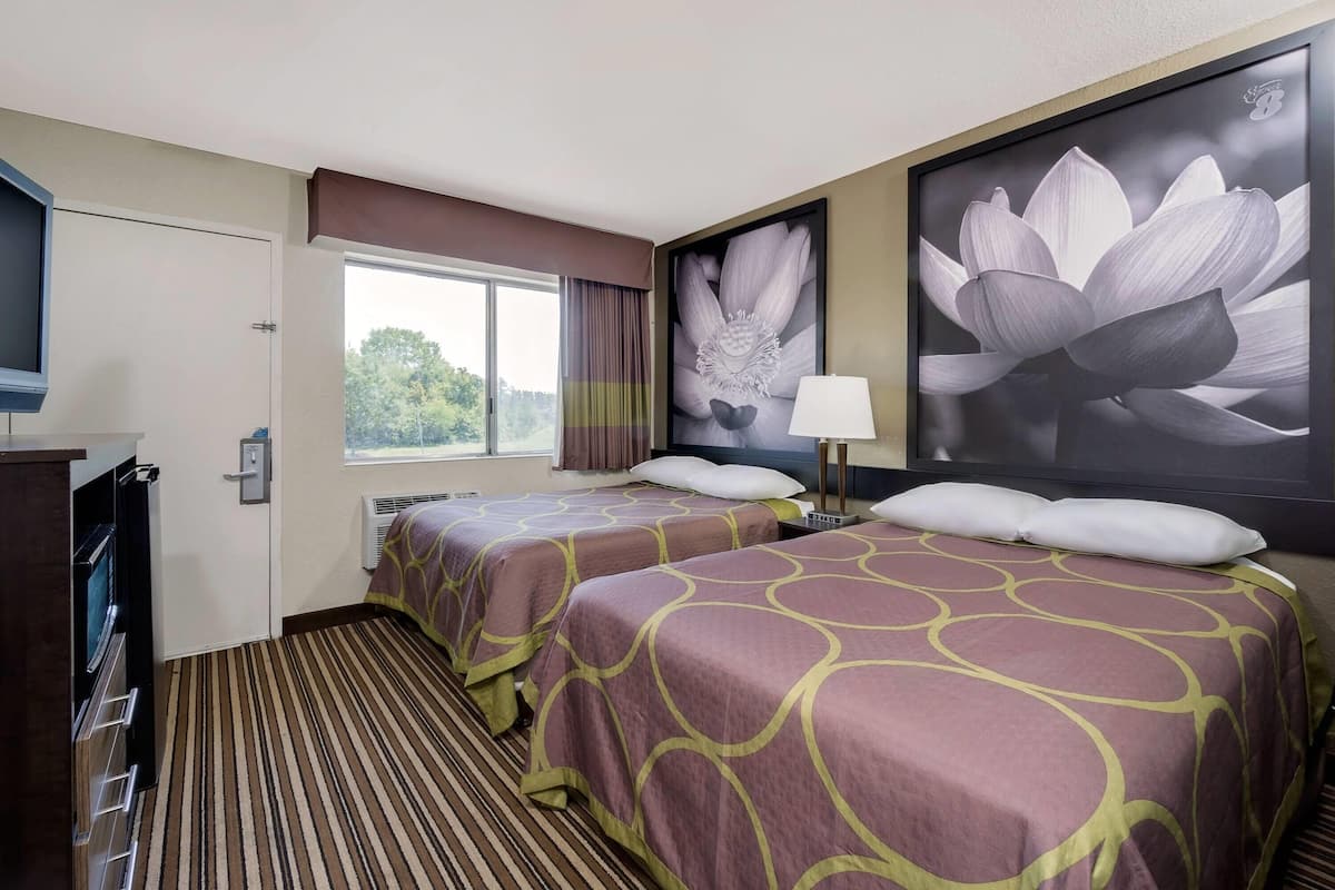 A hotel room with two beds, a TV, a window with curtains, and a large flower painting on the wall.