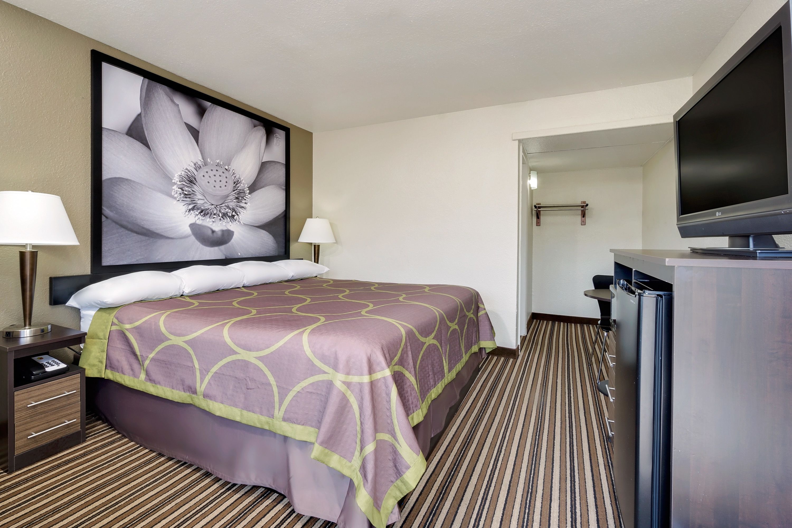A hotel room with a large bed, two bedside lamps, a flat-screen TV, and a framed floral artwork on the wall.