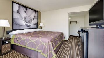 A hotel room with a large bed, two bedside lamps, a flat-screen TV, and a framed floral artwork on the wall.