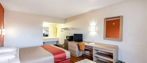 A hotel room with two beds, a desk, a chair, a TV, and a small trash bin.