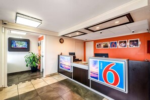 A hotel reception area with a large '6' sign, a digital screen displaying a map, and a clock on the wall. - Motel 6 Anniston, AL (Oxford)