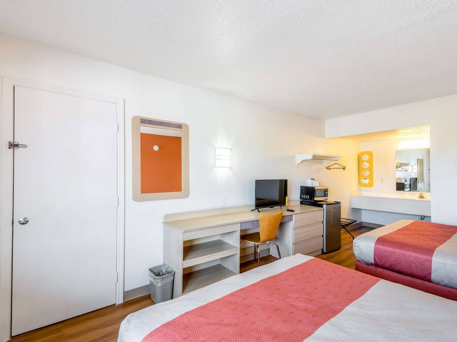 A hotel room with a bed, a desk with a computer, a chair, a TV, and a small kitchenette.