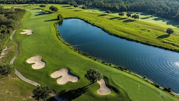 An aerial view of a golf course with sand bunkers, a water body, and surrounding greenery.