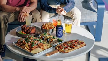 Una mesa con nachos, tacos y pizza, además de bebidas y una botella de cerveza.