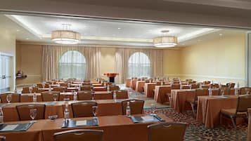 A conference room with multiple tables and chairs, large windows, and a podium.