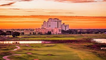 A large hotel with multiple buildings, a golf course with sand bunkers, and a body of water reflecting the sky.