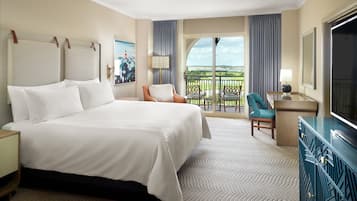 A hotel room with a large bed, a desk with a TV, a chair, a balcony with a view, and a painting on the wall.