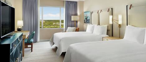 A hotel room with two beds, a TV, a desk, and a view of the outdoors.
