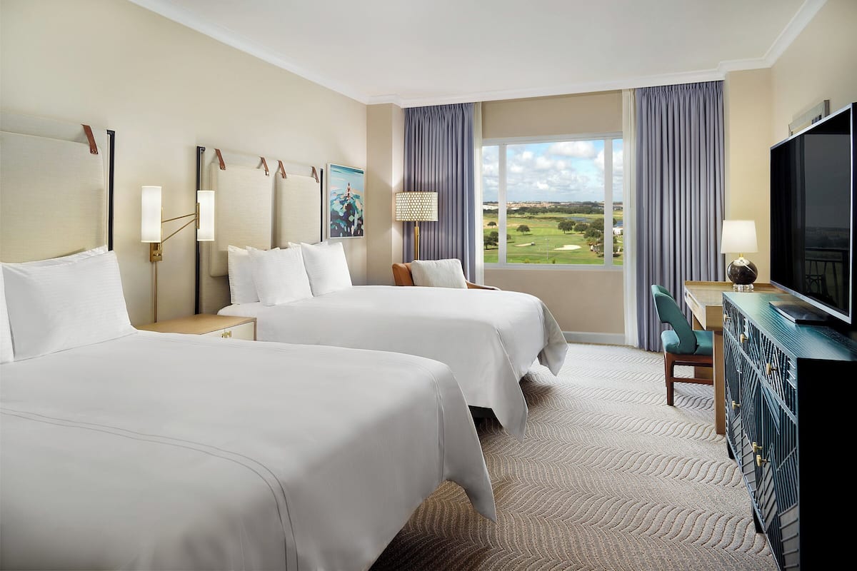 Une chambre d’hôtel avec deux lits, un bureau, une télévision et une vue sur un terrain de golf.