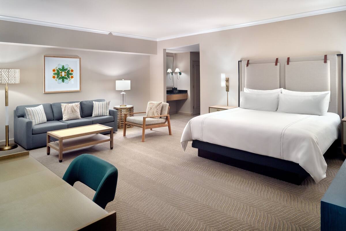 Une chambre d’hôtel avec un lit, un canapé, une chaise, un bureau et une salle de bain visible à travers une porte ouverte.