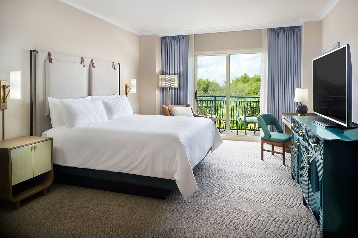 Une chambre d’hôtel avec un grand lit, une télévision, un bureau et un balcon donnant sur un paysage verdoyant.