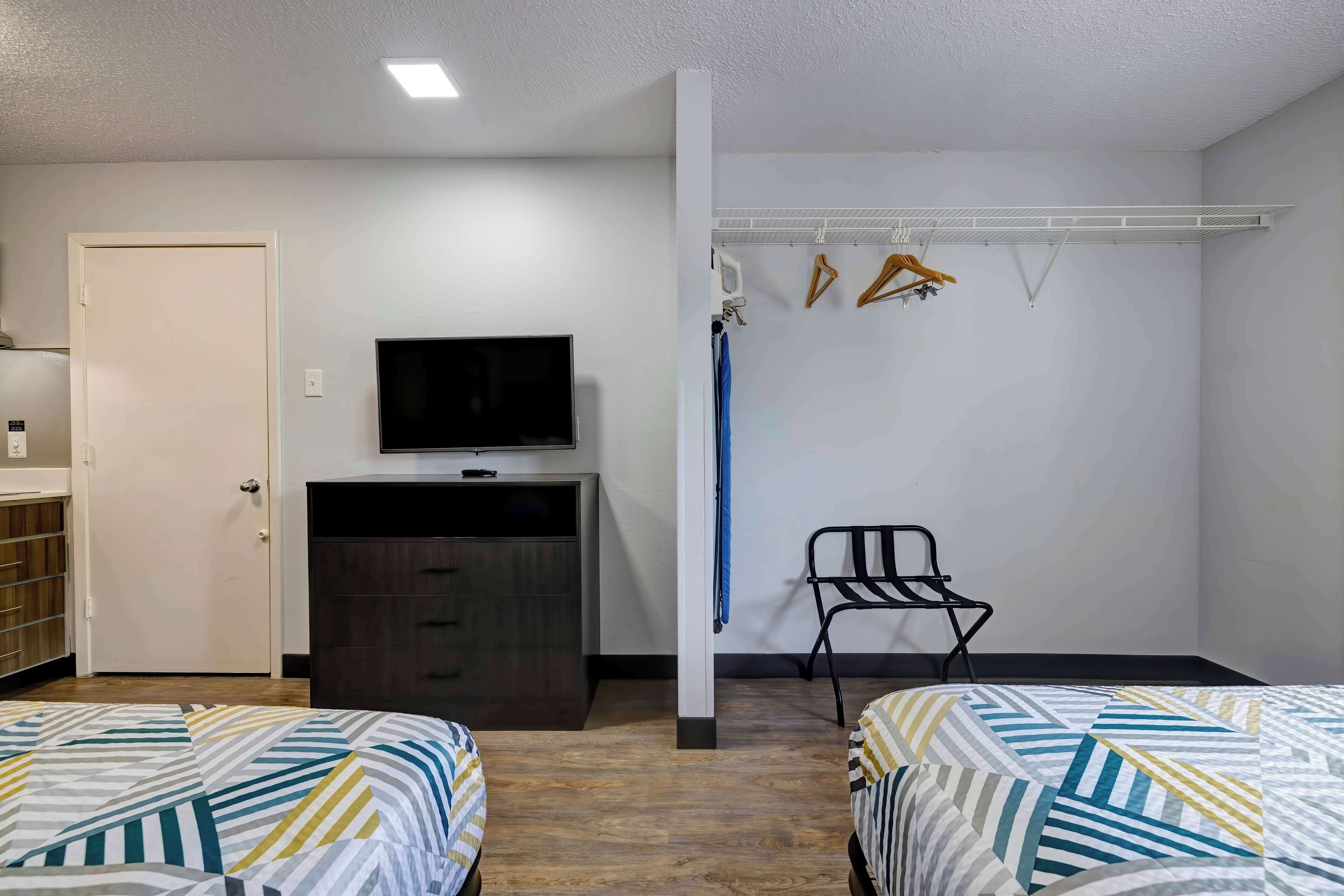 Une chambre d’hôtel avec deux lits, un téléviseur posé sur une commode, une chaise et un porte-manteau avec des cintres.