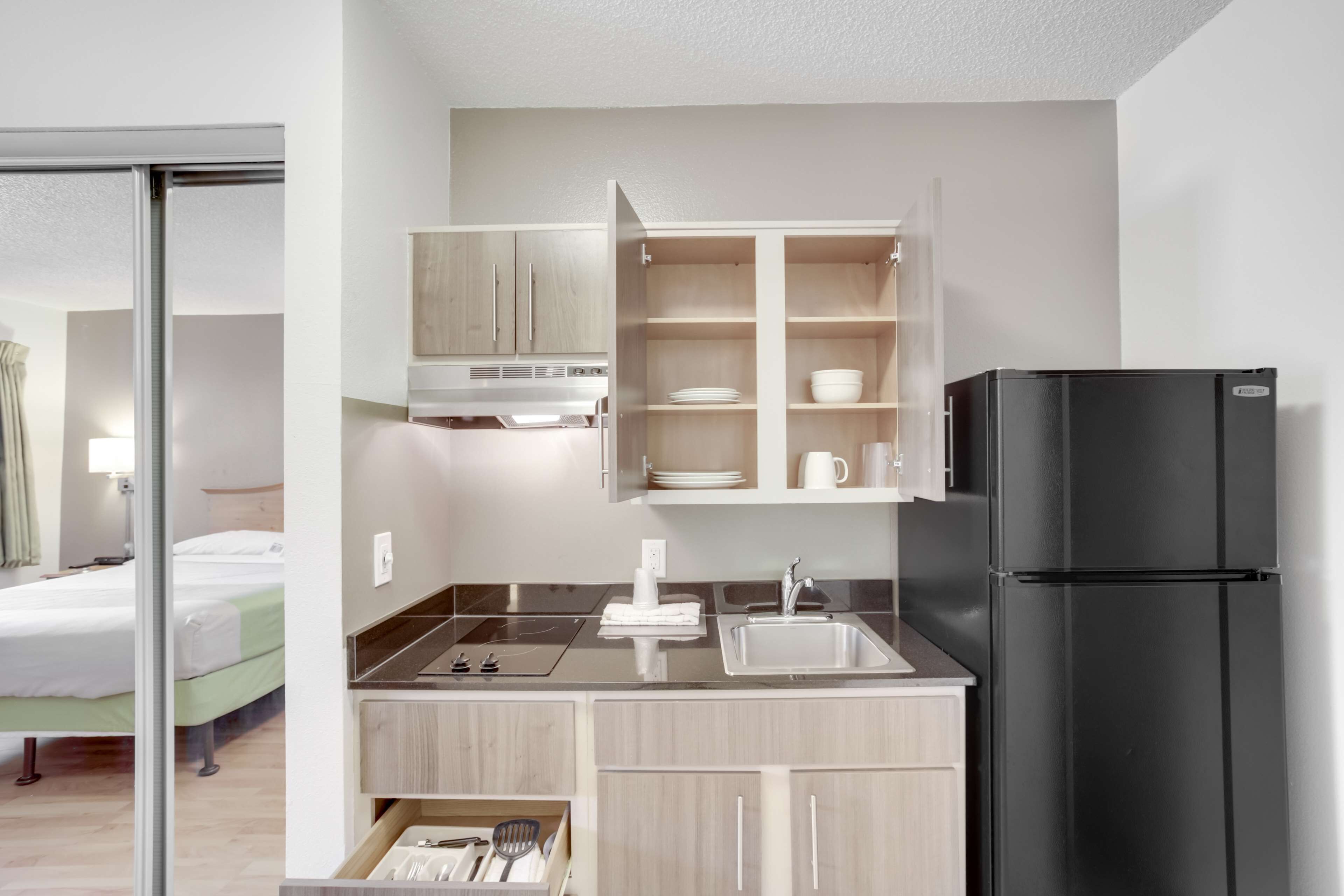 A compact kitchenette with a black refrigerator, a sink, and a built-in oven. There is a small countertop with a dish rack and a cabinet above it.