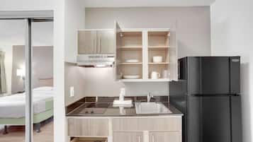A compact kitchenette with a black refrigerator, a sink, and a built-in oven. There is a small countertop with a dish rack and a cabinet above it.