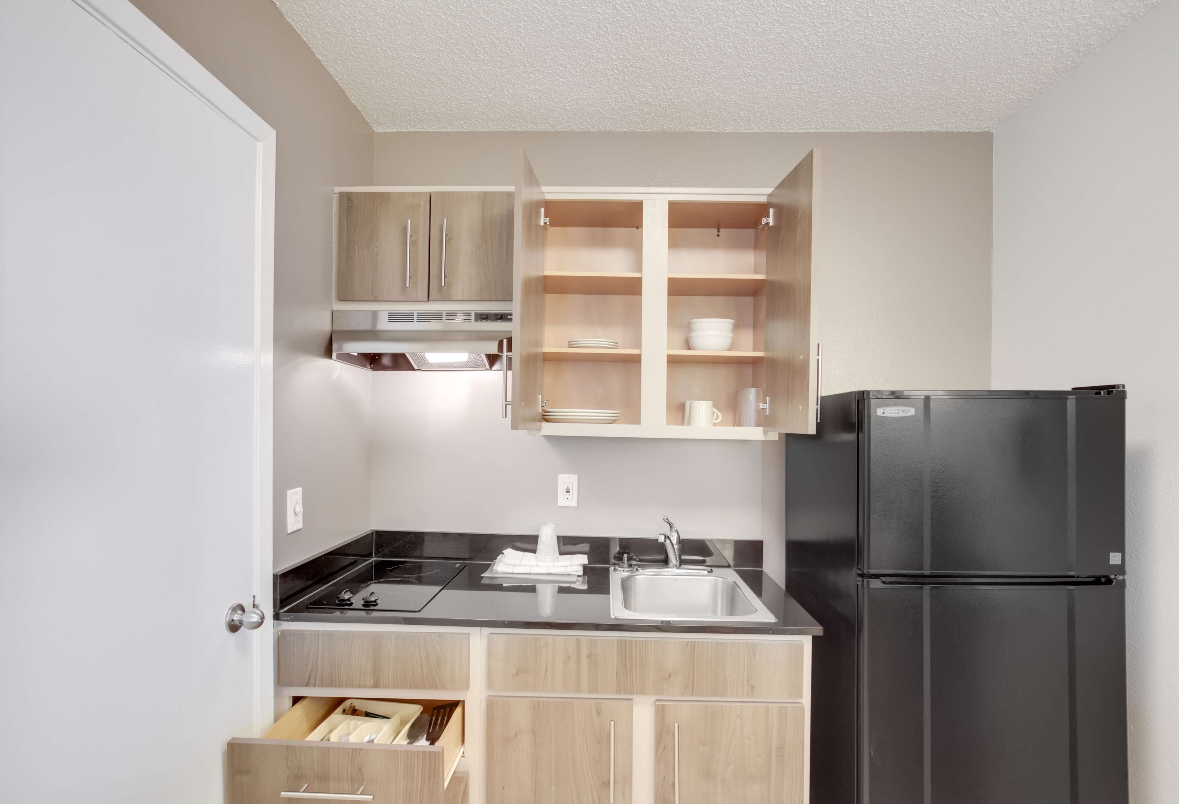 A compact kitchen with a black refrigerator, a sink, and wooden cabinets.