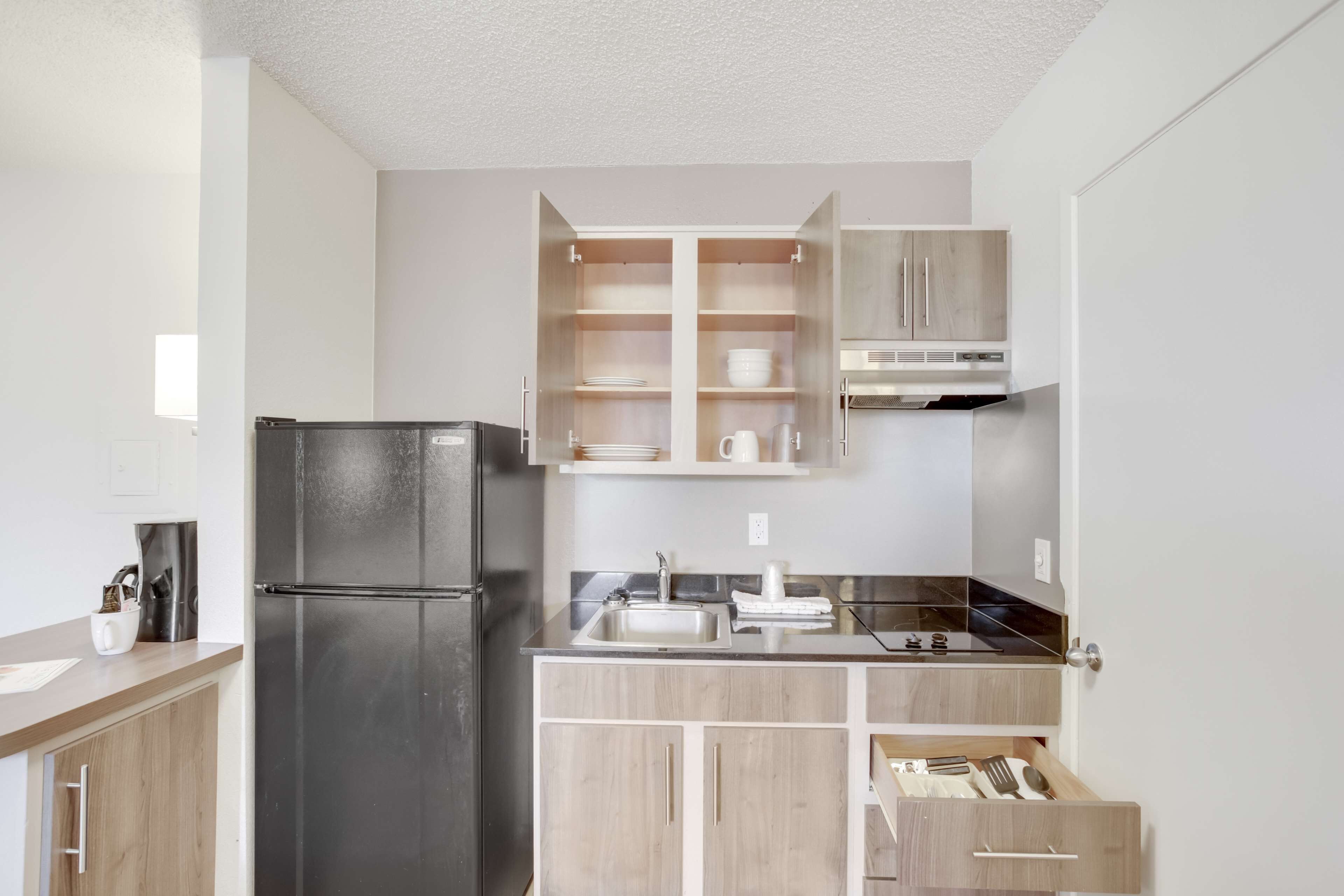 A compact kitchen with a black refrigerator, wooden cabinets, a stainless steel sink, and a microwave.