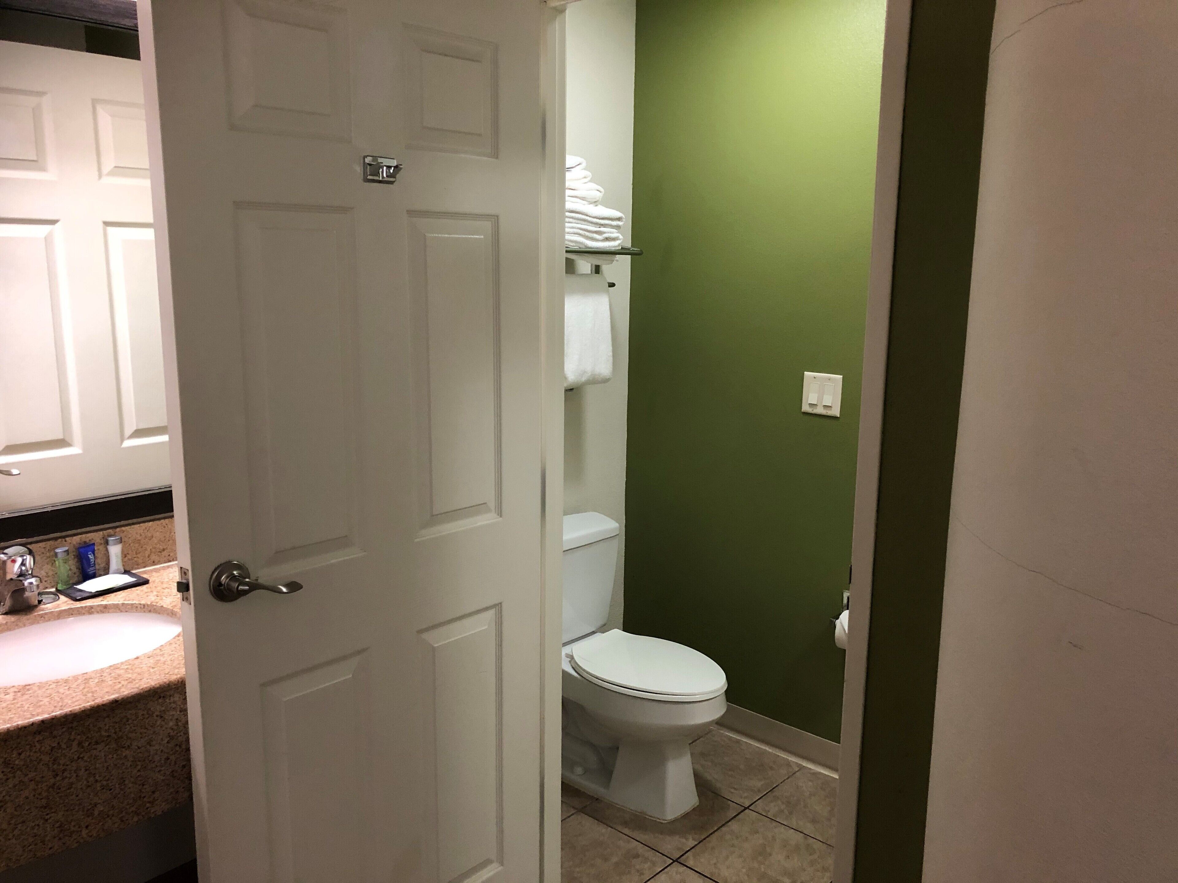 Un baño con inodoro blanco, paredes verdes y lavamanos blanco con artículos de aseo.