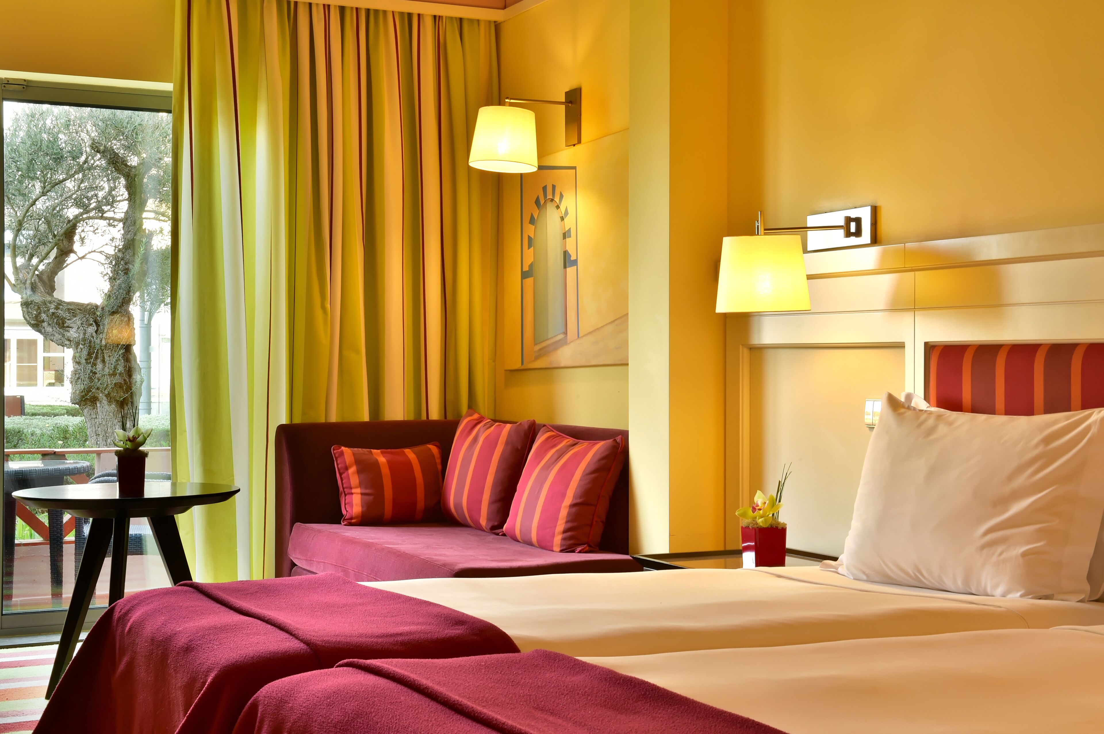A hotel room with a bed, two bedside tables, a sofa, and a window with curtains.