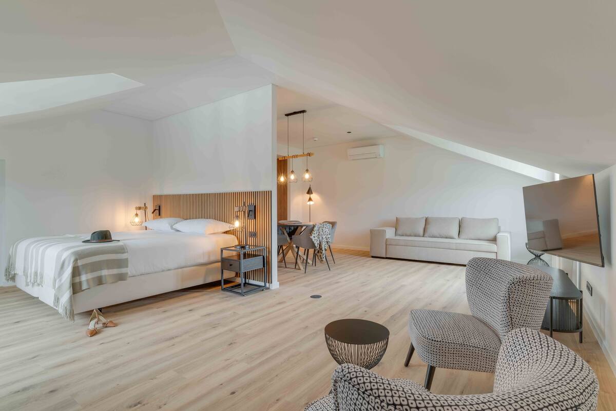 Quarto de hotel moderno com uma cama grande, um sofá, uma TV e um espaço de refeições.