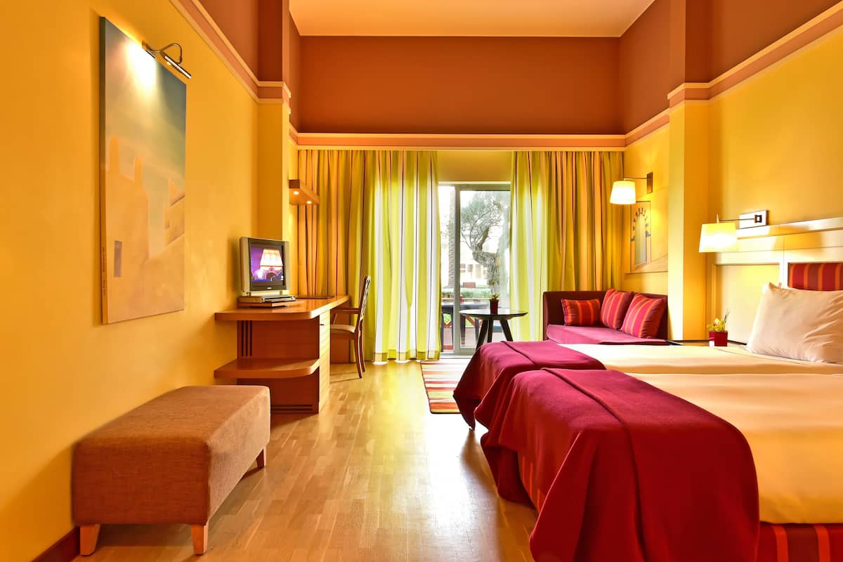 Quarto de hotel com duas camas, uma escrivaninha, uma cadeira e uma mesinha.