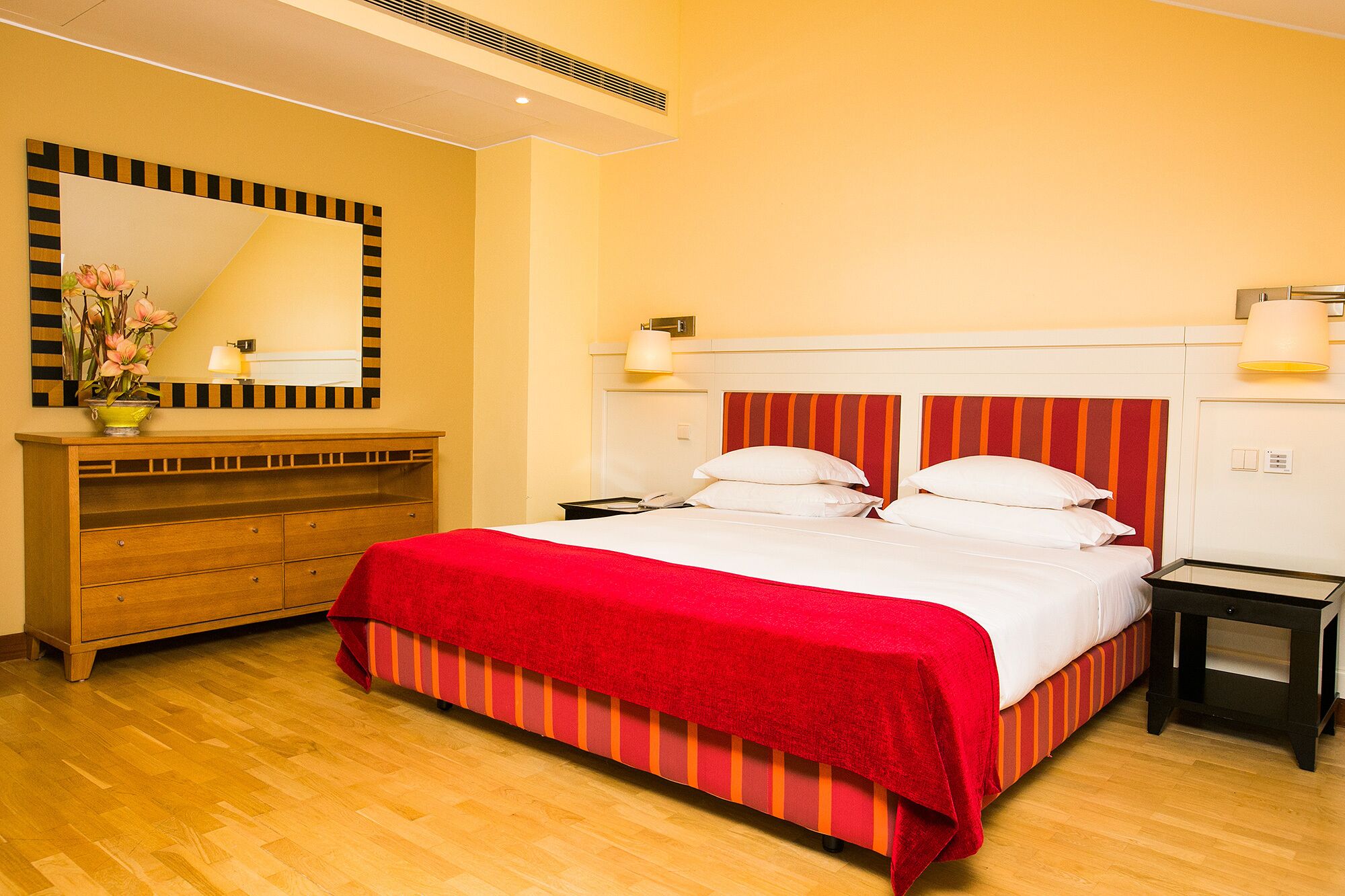 A hotel room with a large bed, wooden dresser, and a mirror with a decorative frame.