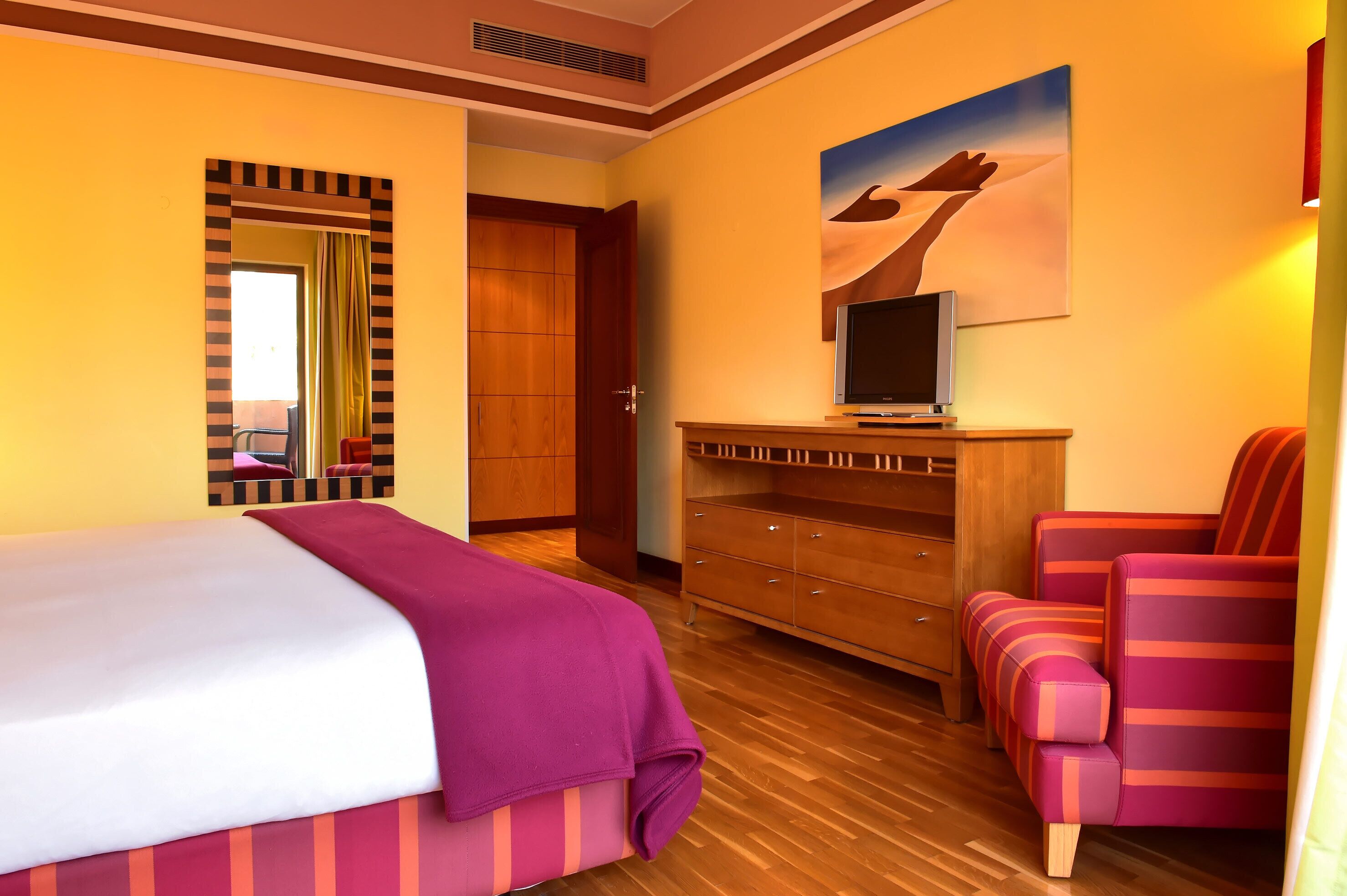 A hotel room with a bed, a wooden dresser, a TV, and a chair.