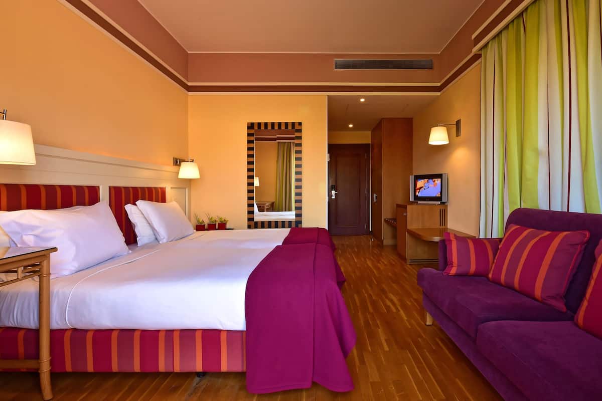 Quarto de hotel com cama, sofá, televisão e banheiro visível por uma porta.