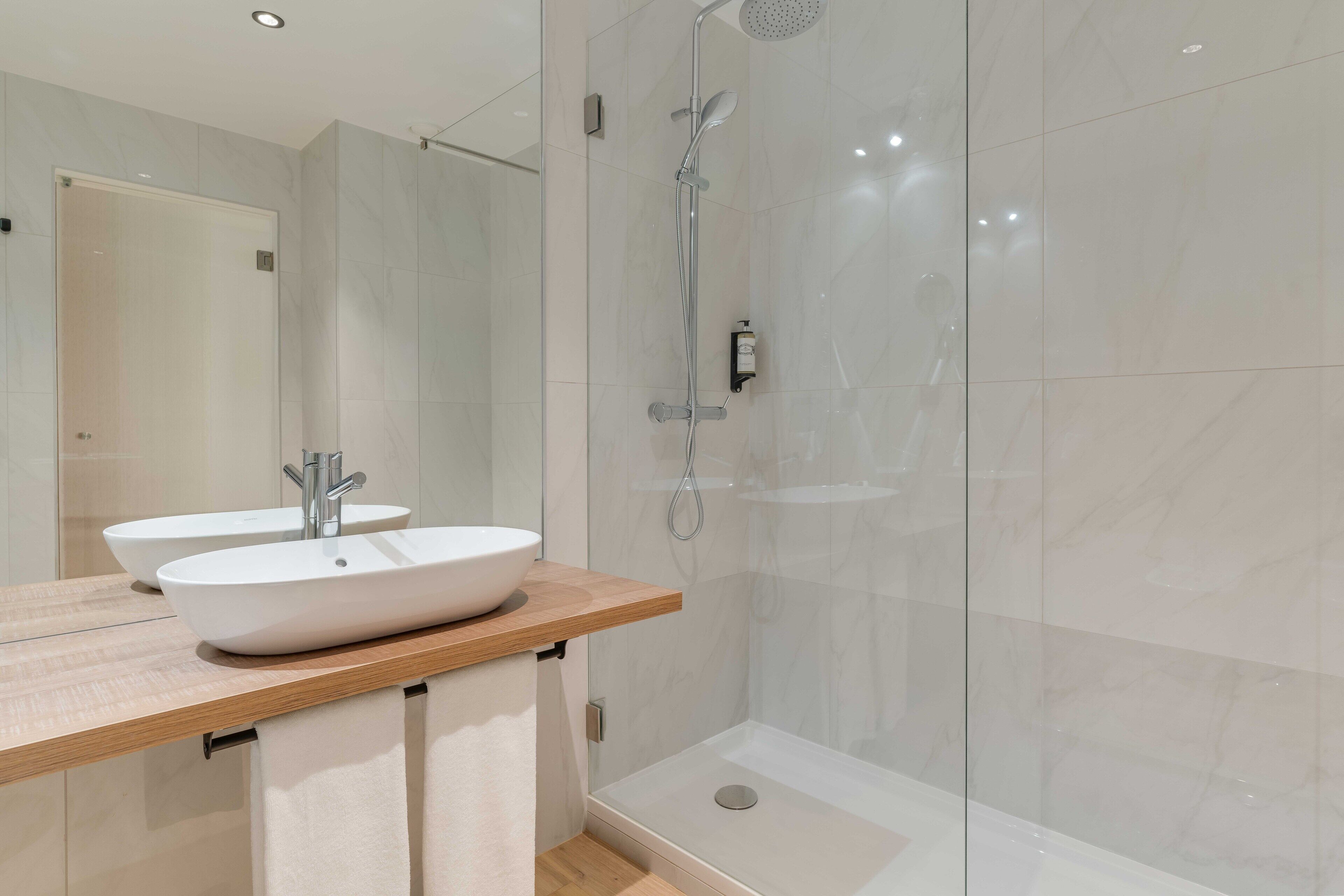 Un baño moderno con un espejo grande, dos lavamanos y una ducha a ras de suelo.