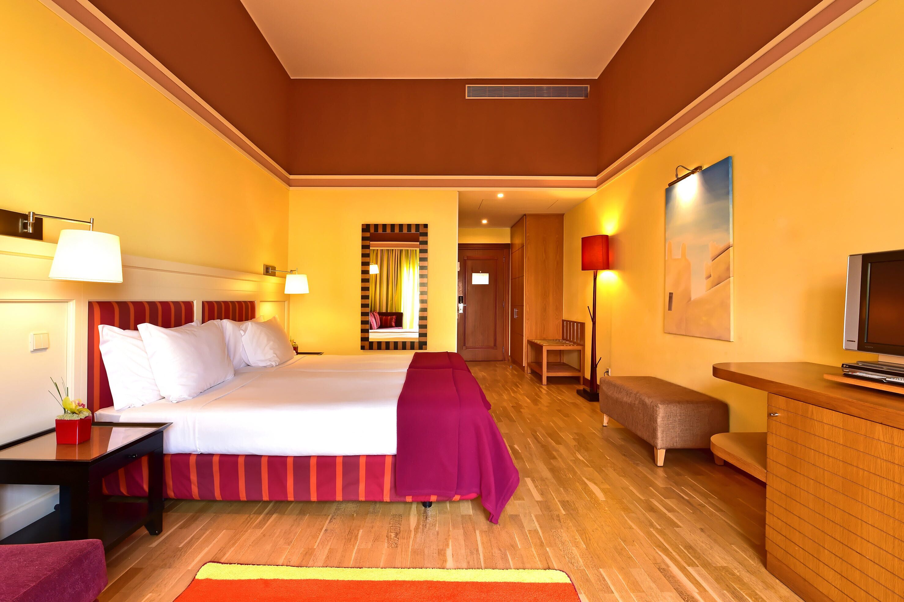 Une chambre d’hôtel avec un grand lit, des tables de chevet, un bureau, une chaise, une télévision et un miroir.