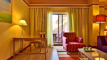 A hotel room with a wooden table, a striped armchair, a sofa, and a glass coffee table with apples.