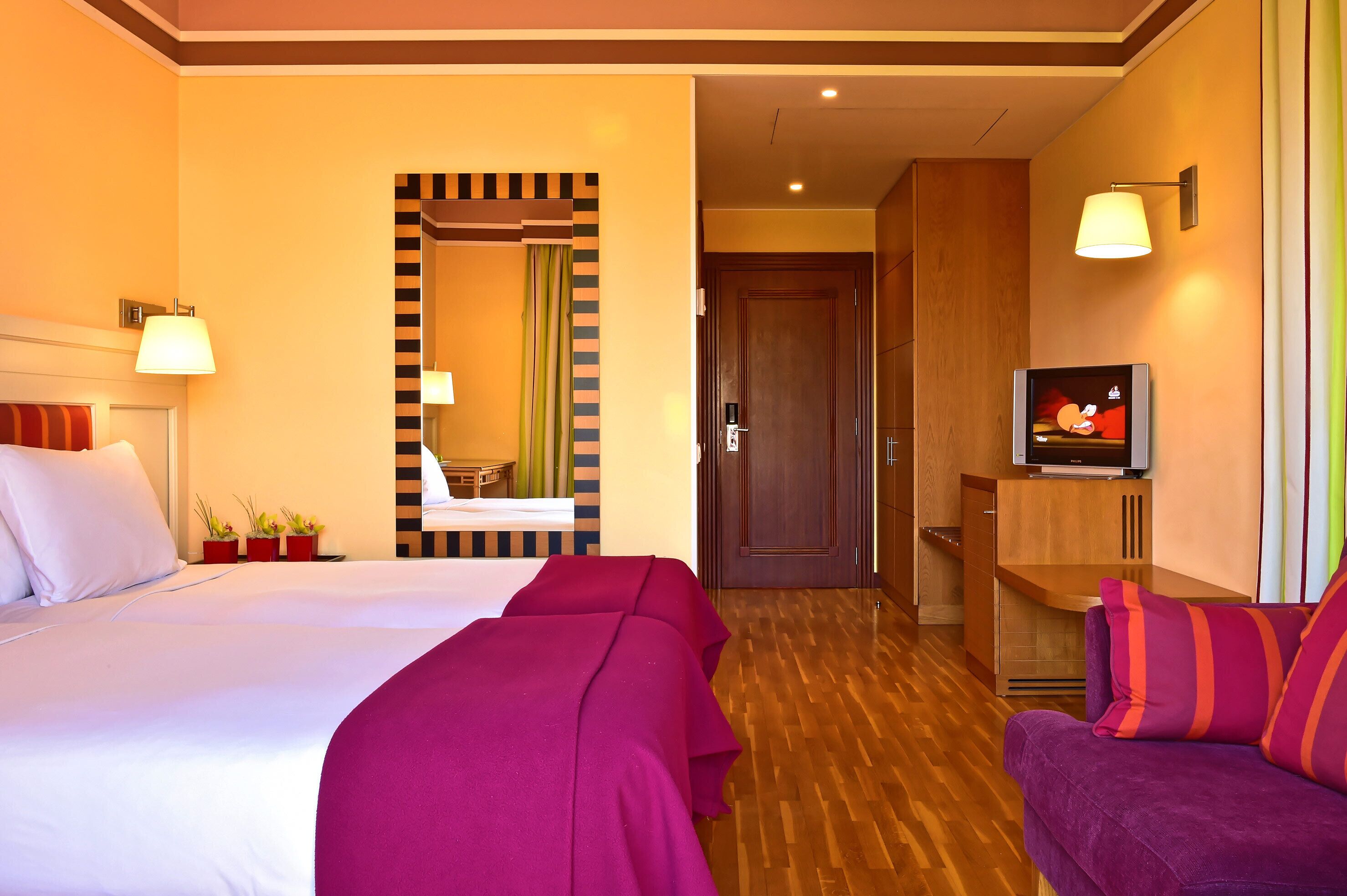 A hotel room with a bed, two bedside tables, a TV, a sofa, and a mirror.