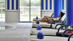 A lounge area with a person relaxing on a chair, a stone wall, and a glass door leading outside. - Pestana Sintra Golf Conference & Spa Resort (Sintra)