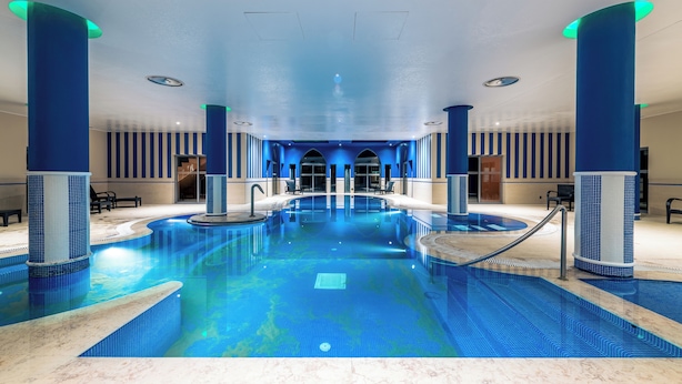 An indoor swimming pool with blue-tiled walls and columns, surrounded by seating areas and a clear view of the pool. - Pestana Sintra Golf Conference & Spa Resort (Sintra)