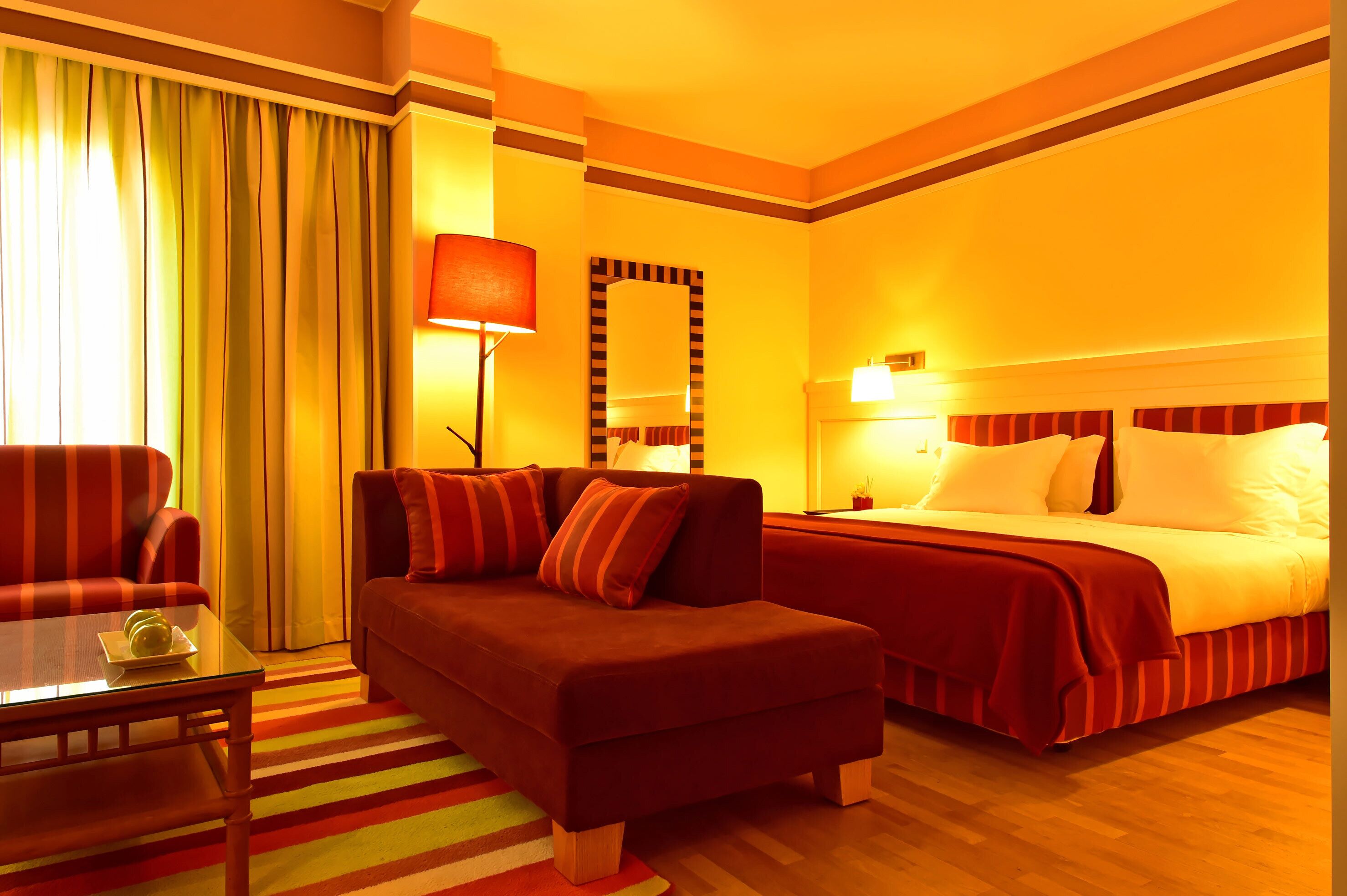 A hotel room with a sofa, a bed, a table, and a mirror.
