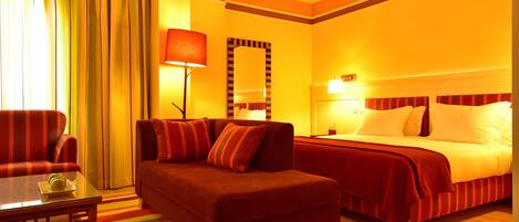 A hotel room with a sofa, a bed, a table, and a mirror.