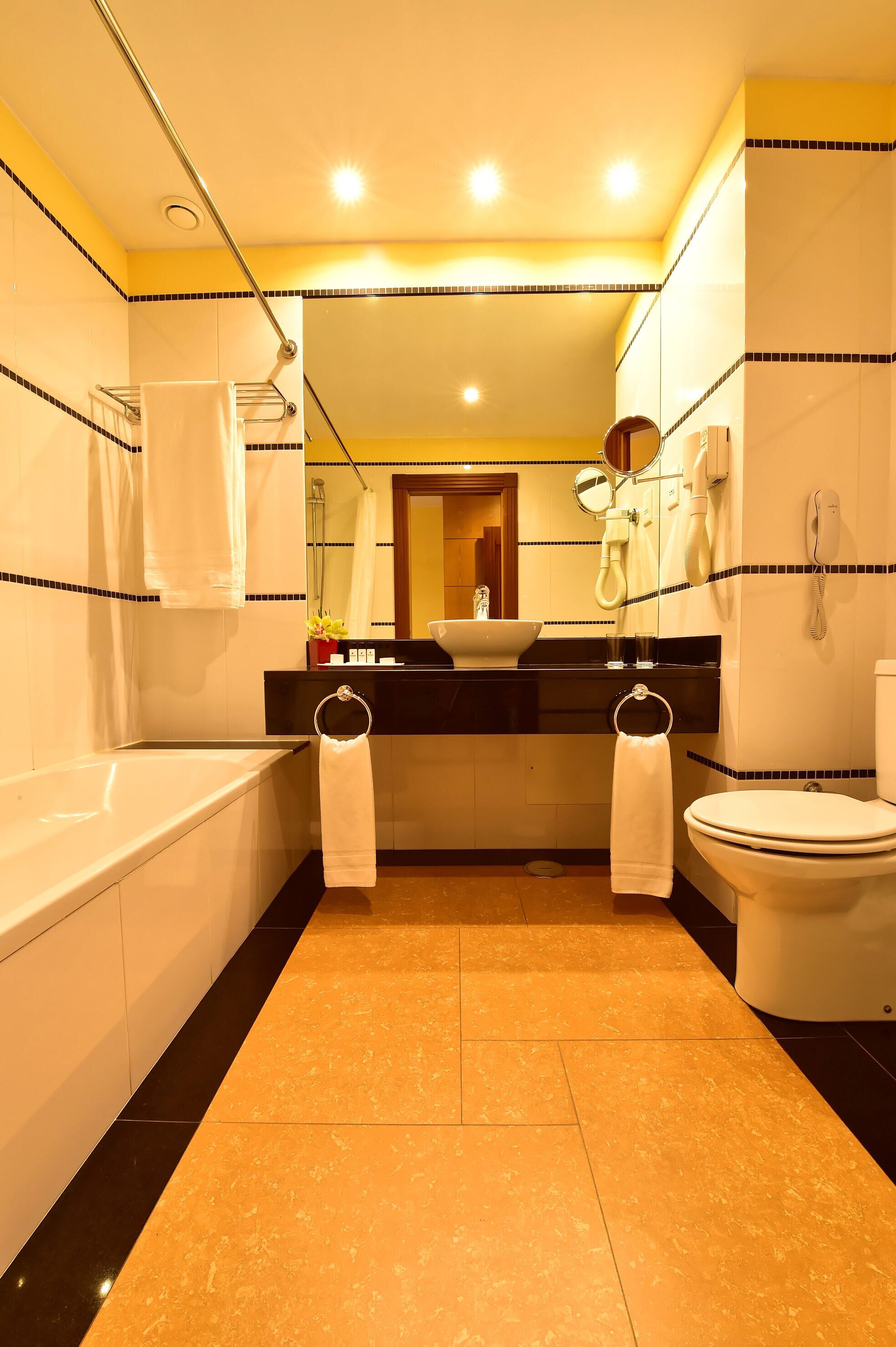 A modern bathroom with a bathtub, toilet, and sink. There are two towels hanging on towel rings. The floor is tiled, and the walls have a decorative border.