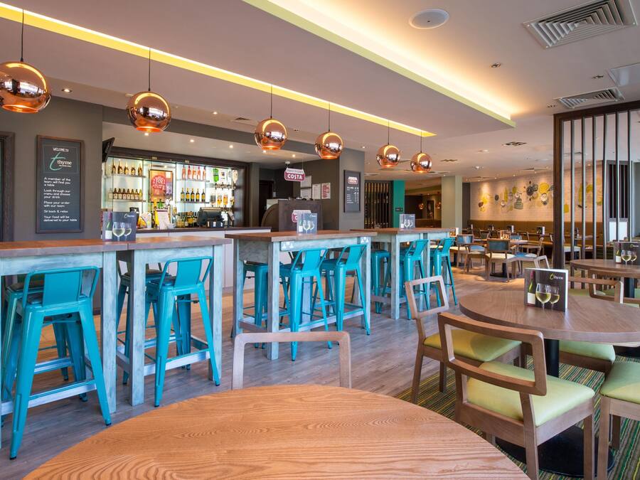 A modern bar area with round tables, teal chairs, and pendant lighting.