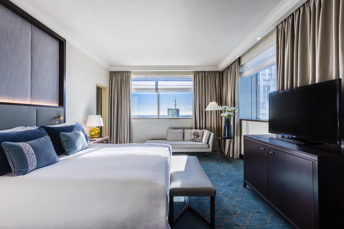 Una camera d'hotel con un letto grande, un divano, una televisione e vista sullo skyline cittadino.
